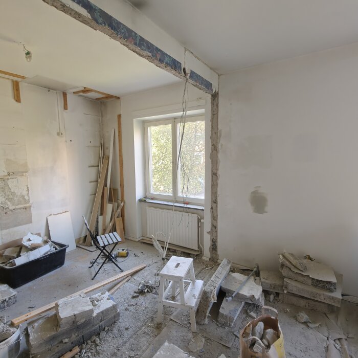 Renovering med delvis borttagen vägg i lägenhet, innehållande slaggbetongblock, ställning, verktyg och byggmaterial i rummet.