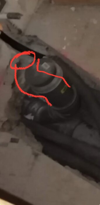 Rörinstallation med t-koppling och rödmarkerad böj för eventuell justering vid rörläggning. Synligt betonggolv och omgivande material.