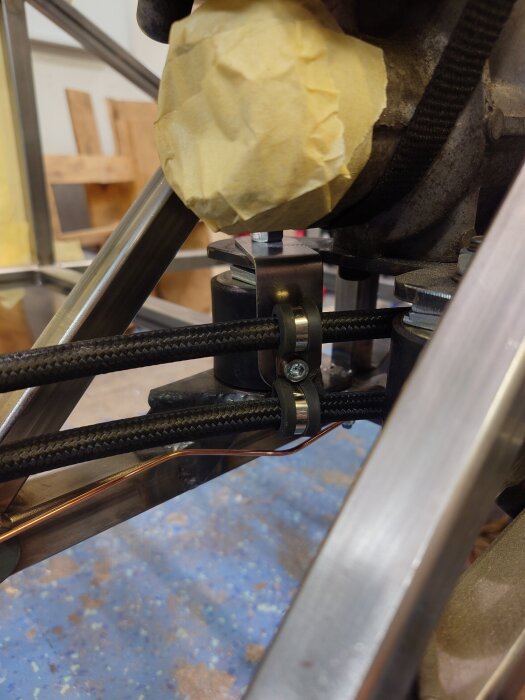 Fäste för bränsleslang med AN-koppling installerad på metallram, omgiven av mekaniska komponenter i verkstadsmiljö.