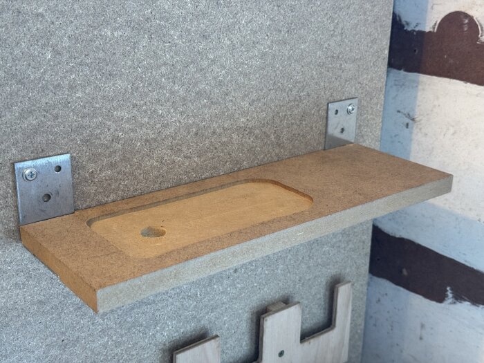 En monterad väggshylla med urtag för en sticksåg, tillverkad av träskivor, med metallbeslag för upphängning.