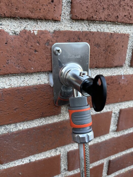 FM Mattsson g15 utkastare installerad på en tegelvägg, med en koppling och slang ansluten. En nyckel sitter i ventilen.