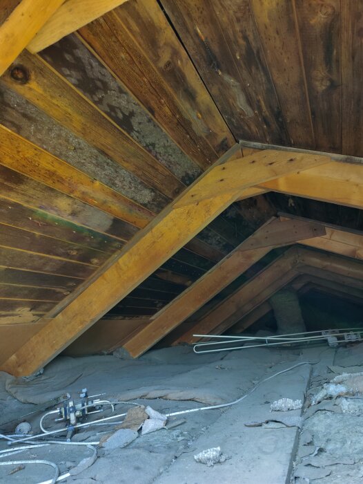 Svartnad råspont i ett vindsutrymme, med synliga bjälkar och isolering. Byggprojekt pågår med bedömning av träets skick.