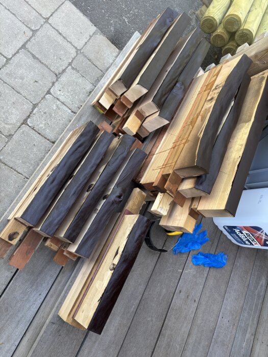 Brädor med bränt, borstat och betsat råkant ligger staplade på trätrall med blå handskar bredvid.