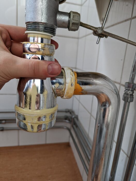 En person håller en del av avloppsröret och vattenlåset under ett tvättställ, med fokus på anslutningen där det läcker.