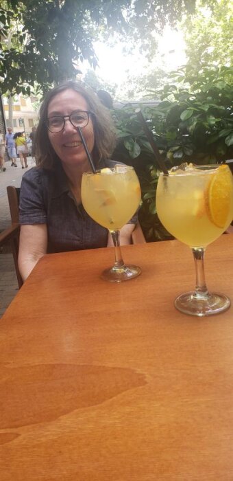 Två glas sangría med cava, dekorerade med apelsinskivor, står på ett bord utomhus, med grönska i bakgrunden.