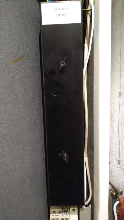 Svart styrenhet märkt "CL300" med synliga kablar, monterad inomhus på en vägg.