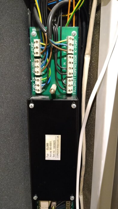 Närbild på ett styrkort med flera anslutna kablar, märkningar för pumpar och kompressor syns. En svart box med etikett nederst.