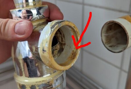 Hand håller i ett rör med gängor, pilar markerar en del som saknas på en kromad VVS-koppling i ett kök.