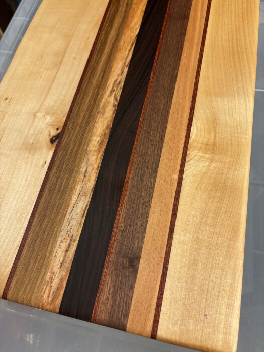 Skärbräda med ränder av olika träslag som lönn, ek och valnöt. Brädan har en tydlig råkant och behandlats med bets och paraffinolja.