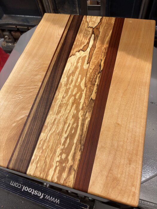 Skärbräda av lönn, rötad lönn och andra träslag, accentuerad med svart bets, med varierande träfärg och struktur.