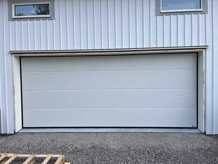 Garagedörr monterad på vit byggnad, omgiven av klart foder och ny snickrad portinklädnad.