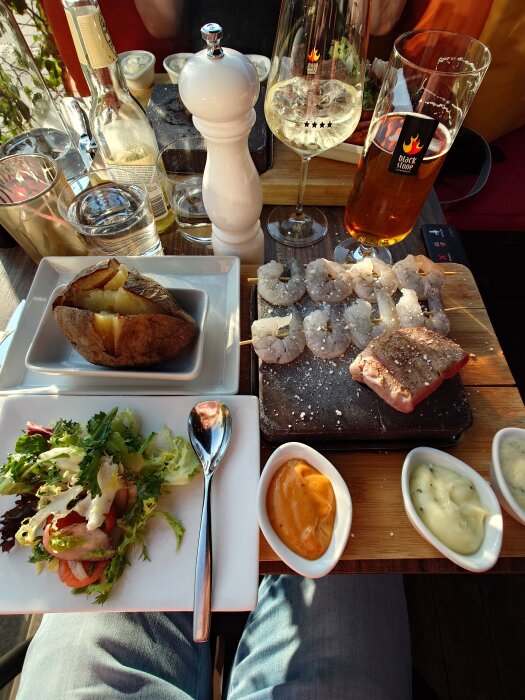 Surf and turf middag med kalvbiff och wannameiräkor, bakad potatis, sallad och såser. Vin och öl på bordet. Bröllopsdagsfirande.
