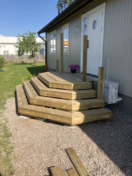 En nybyggd, oavslutad trätrappa vid ett hus, utan räcke, med några brädor kvar på marken bredvid.