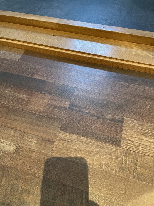 Hög tröskel till badrum täckt med eklist, golvet syns med skuggor.