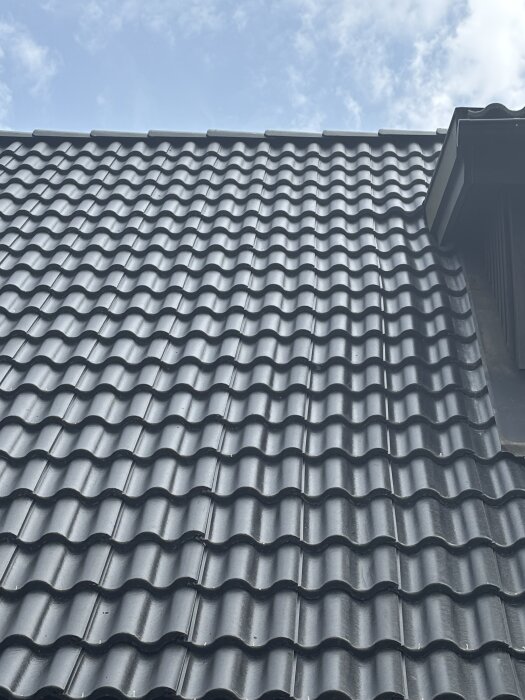 Tak med nyligen bytta takpannor som verkar vara ojämnt monterade, fotat mot en blå himmel.