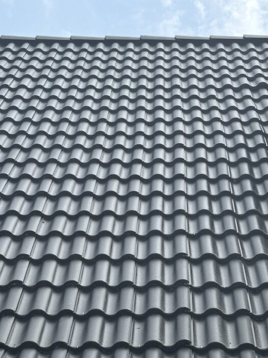 Tak med svarta takpannor, oregelbundna linjer syns.