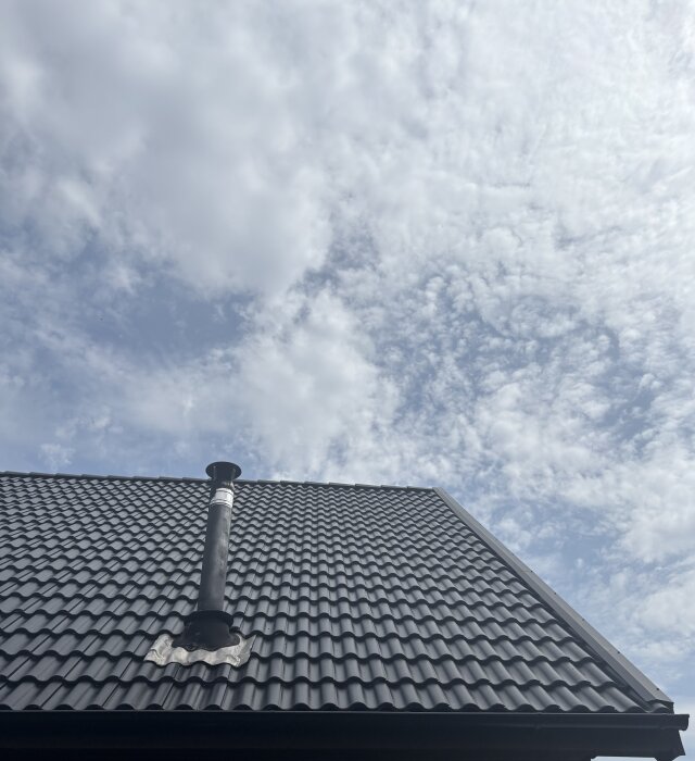 Tegeltak med synliga ojämnheter och luftventil, bildad mot molnig himmel.