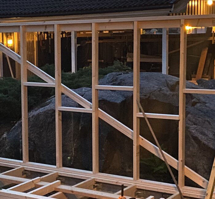 Träram för väggkonstruktion med delade fack för isolering, belägen utomhus nära en stenformation och belysning i bakgrunden.