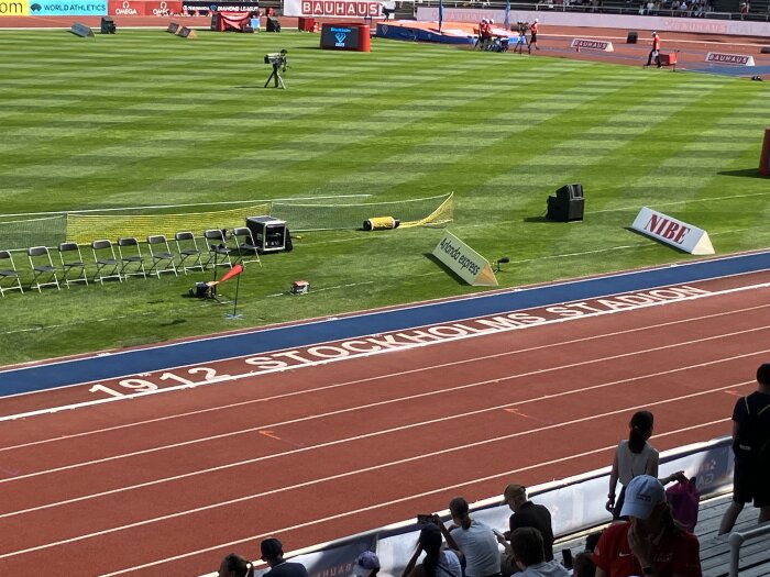 Atletikstadion med grön gräsplan, löparbanor och sittplatser. Text på banan: "1912 STOCKHOLMS STADION".
