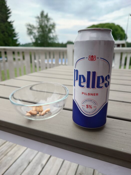 Burk med öl märkt "Pelles Pilsner" och en glasburk med snacks på en träveranda.