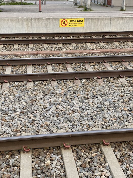 Järnvägsspår med grus och livsfara-skylt som varnar för att beträda spårområdet.