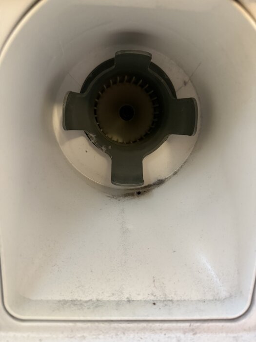 Närbild på en vit trumma eller ventil utan isolering, med en central komponent av grön plast och smutsavlagringar på insidan.