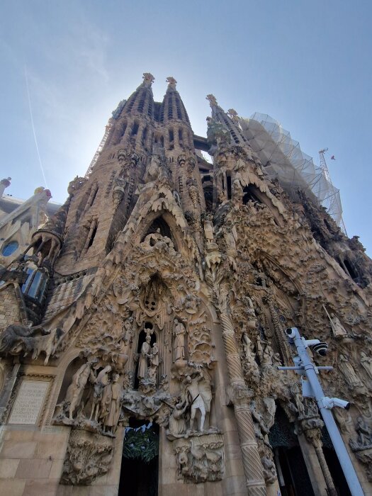 En del av en gotisk katedral med höga spiror och detaljerade stenreliefer under en blå himmel.