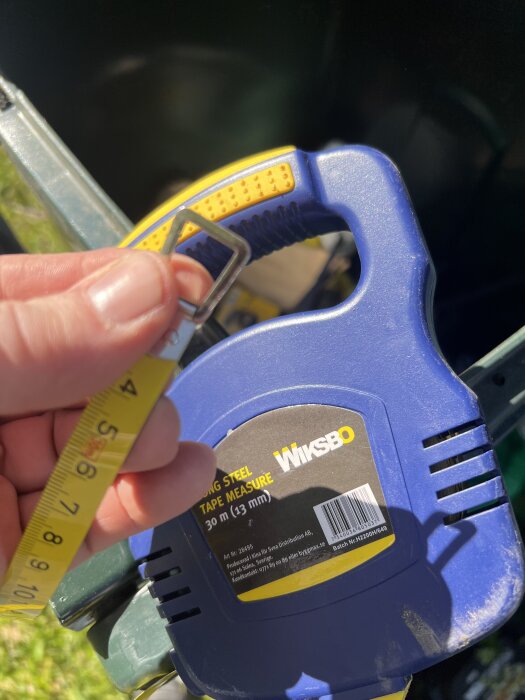 Gult och blått måttband med handtag märkt med "Wiksbo", hålls över en grön bakgrund.