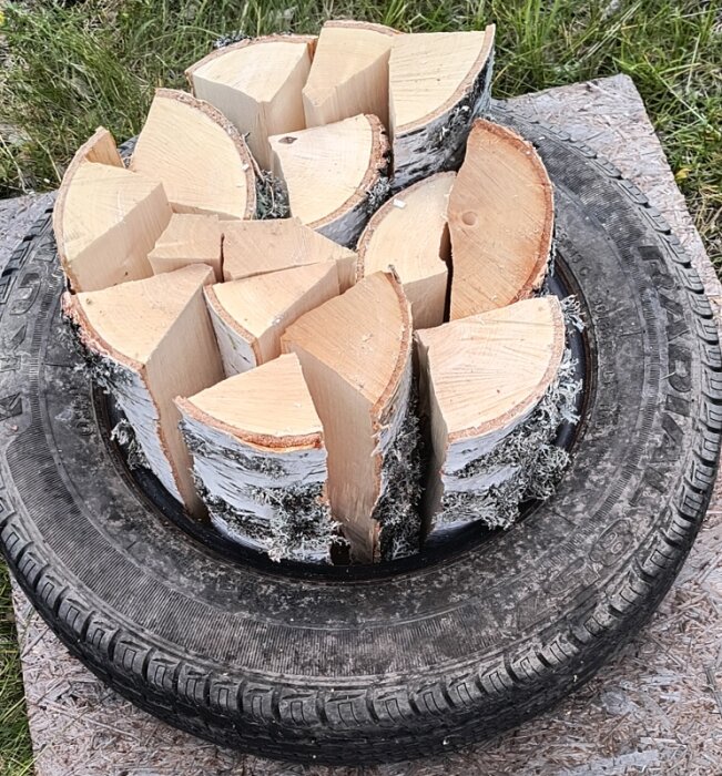 Vedträn staplade i en cirkel inom ett gammalt bildäck på en träskiva.