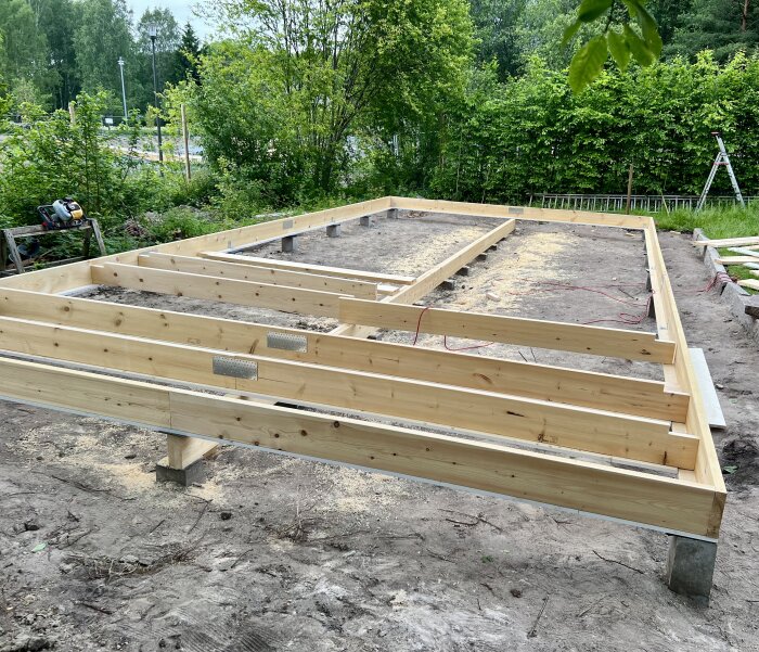 Träram byggs på en jordtomt, omgiven av grönska.