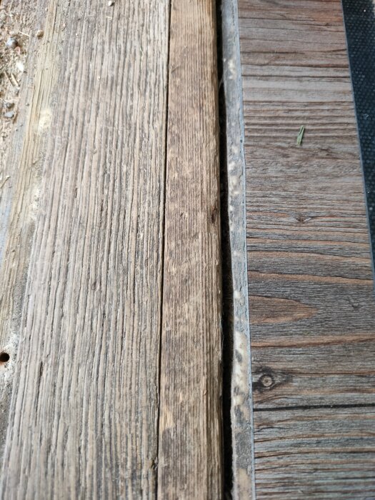 Övergång mellan trätröskel och vinylgolv med en synlig skarv där smuts samlas.