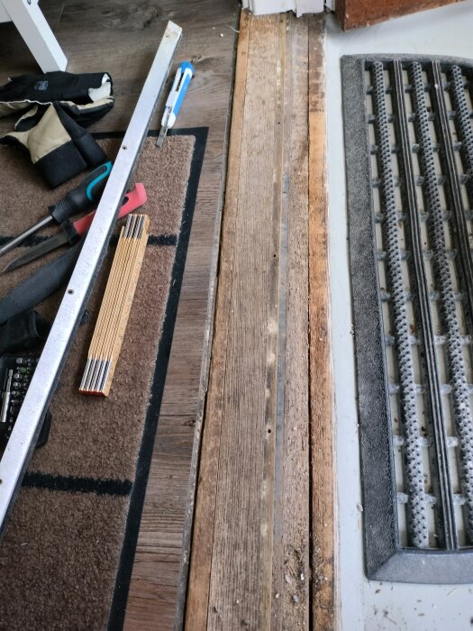 Tröskel vid ytterdörr med verktyg och material, inklusive vinylgolv och en ojämn övergång där smuts samlas, pågående renovering.