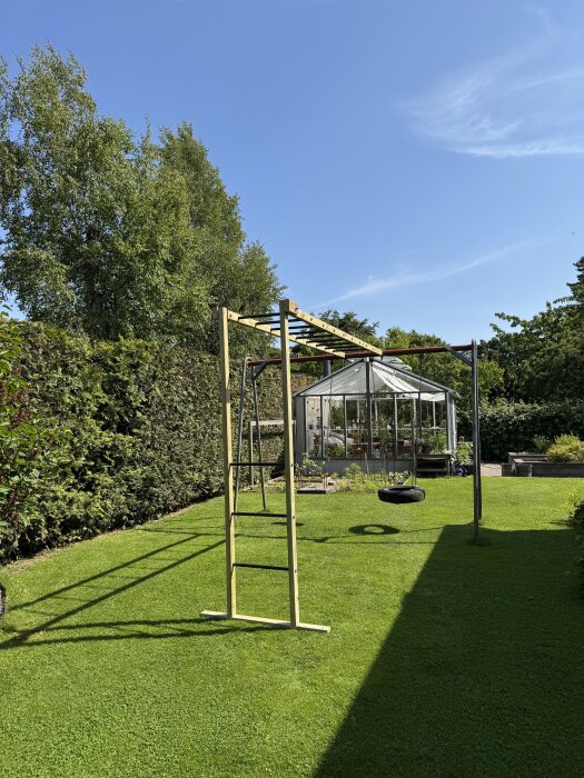 Trädgård med armgångsställning fäst vid gungställning, byggd med trä och metalldelar på en gräsmatta, växthus i bakgrunden.