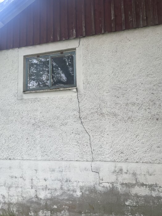 Stor spricka i yttervägg på äldre stallbyggnad, sträcker sig från botten till fönstret, byggt med oklart material.