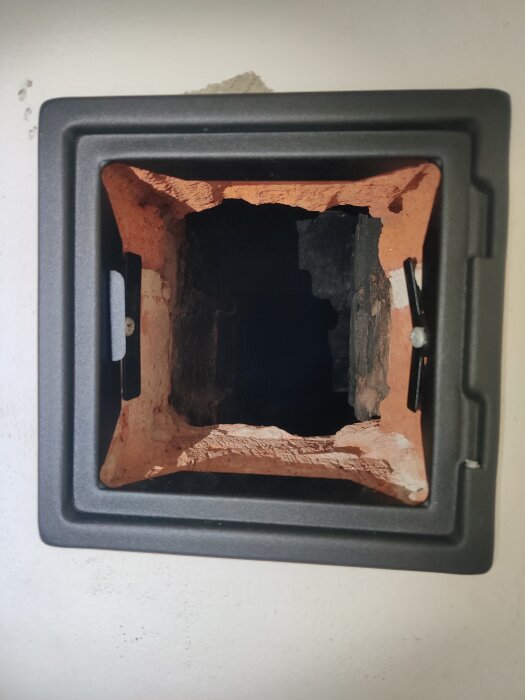 Sotlucka installerad i fritidshusets vägg, omgiven av röd tegel och svart ram.