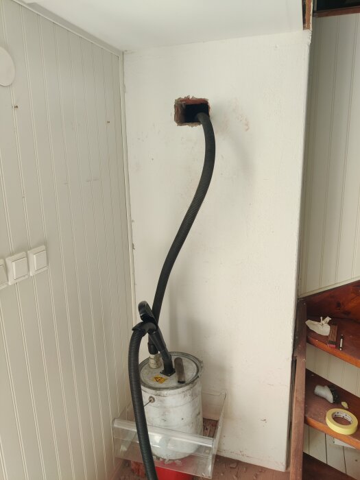 Dammsugare används vid installation av sotlucka i fritidshus, med en slang riktad mot ett nygjort hål i väggen.