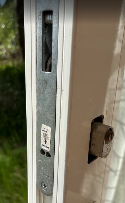 Närbild av en låscylinder monterad på en skjutdörr med en rektangulär platta och skruvhuvuden synliga.