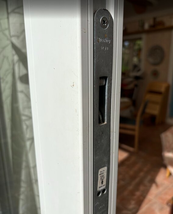 Närbild på ett lås i en skjutdörr, med texten "TrioVing 5149" ingraverad på den metalliska delen monterad i dörrkarmen.