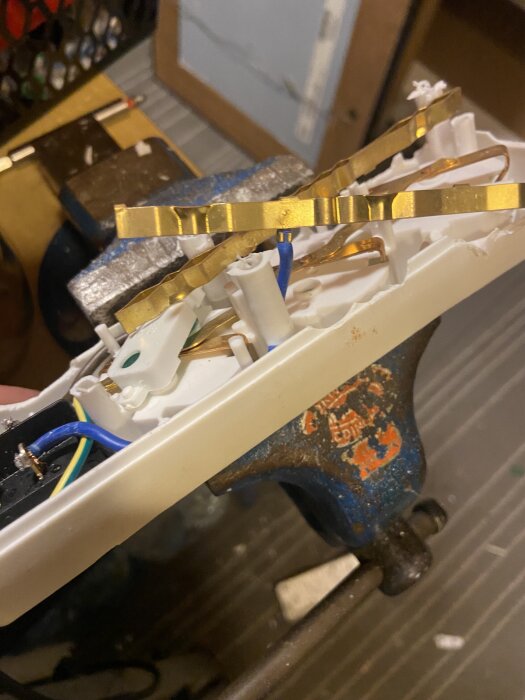 Öppet grenuttag med synliga kopparledningar och kablar, fastspänt i ett skruvstäd, inspekteras för fel.