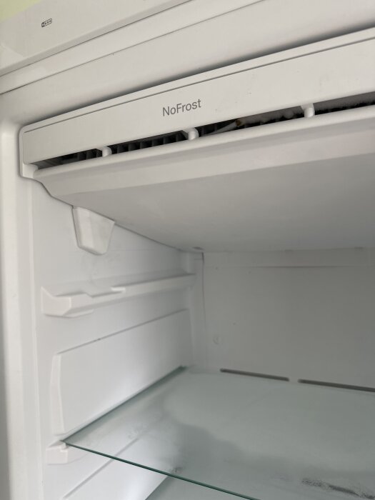 Inuti en frysskåp med NoFrost-teknologi, där en glasplatta syns och det finns tecken på frostbildning.
