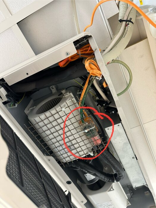 Inuti en takmonterad AC-enhet med kablar och komponenter, en del inringad i rött.