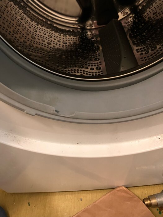 Närbild på en tvättmaskinstrumma med synlig trasig gummibälg på tvättmaskinsluckan.
