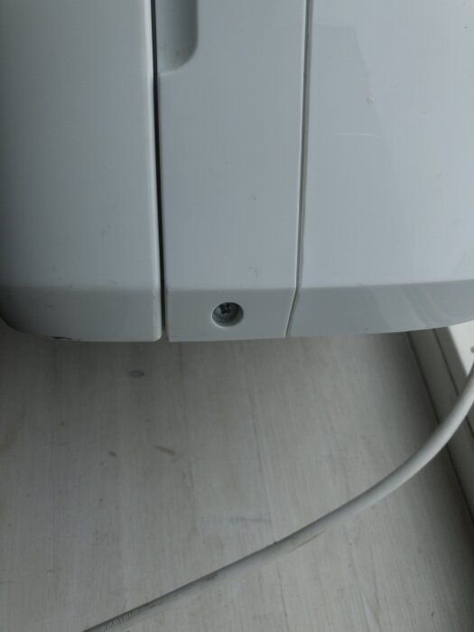 En vit apparat med två paneler och en synlig skruv i ena panelen. Ett elsladd är synligt på sidan.