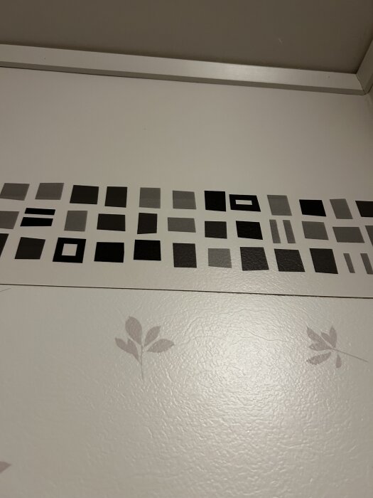 Vägg med våtrumstapet och en överlappande bård i svartvitt rutmönster högst upp.