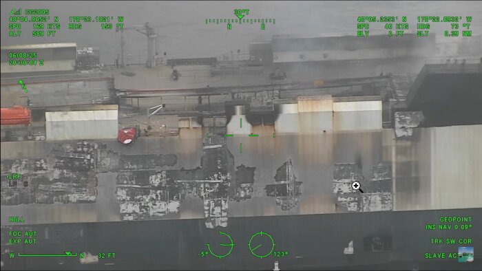 Luftbild av RORO-färja med svarta brännmärken och rökskador, vilket antyder omfattande brand på däcket.