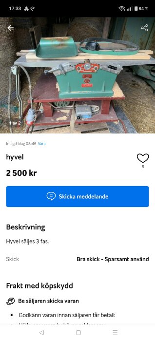Grön hyvel på röd bas, med en skyddskåpa och rem placerad ovanpå, omgiven av höbalar i en lantlig miljö.