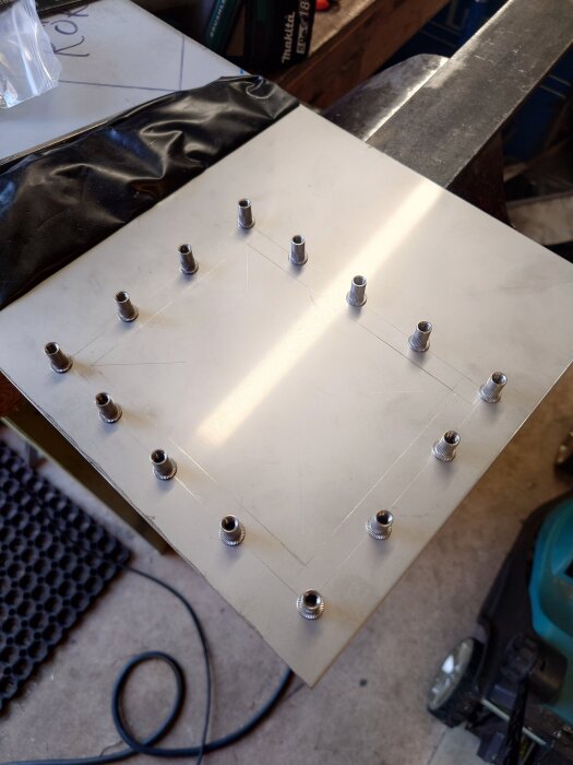 Rostfri stålplåt med flera skruvar i ett rutmönster på arbetsbänk.