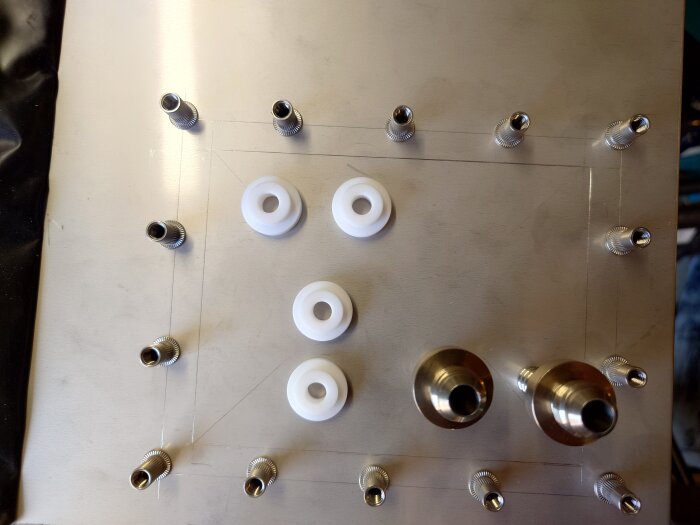 Metallplåt med monterade nitar och fyra vita plastbrickor, verkar representera arbete med 1,5 mm rostfritt stål.