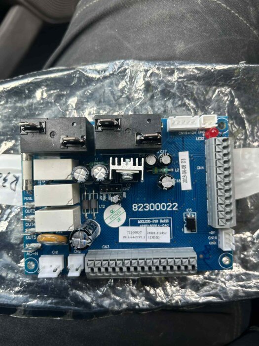 Kretskort för en Hydro Pro P14 värmepump med flera kopplingsterminaler, etiketter och komponenter monterat på en skyddande plastfilm.