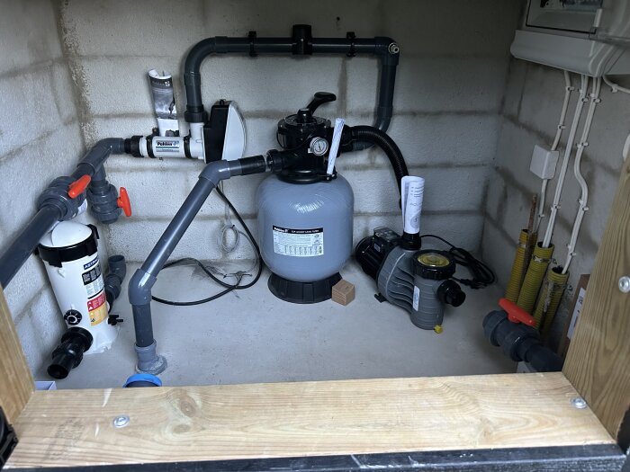 Teknisk installation för poolsystem med pump, sandfilter och rördragning i en liten teknisk kammare.